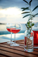 two glasses of rose wine with  olives against blue water on a pier..