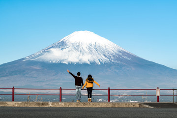 A happy Asian couple hold hand each other looking at big dramatic view of famous mount Fuji in early winter from the hill . Concept of Japan travel with copy space on top.