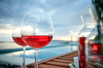 two glasses of rose wine with  olives against blue water on a pier..
