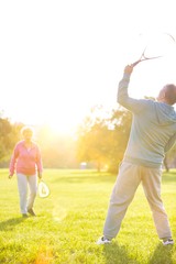 Active senior couple playing badminton in park with yellow lens flare in background