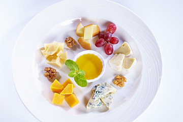 Different type of cheese with honey, grape, nuts on white plate. Top view. Blue cheese, cheddar, parmesan, maasdam and brie cheese slices