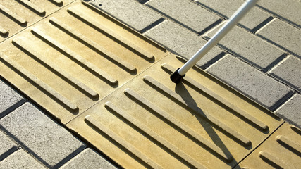 Blind person using white cane on straight tactile tiles to navigate road