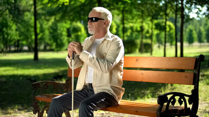 Blind man sitting on bench, listening for sounds in park, heightened senses