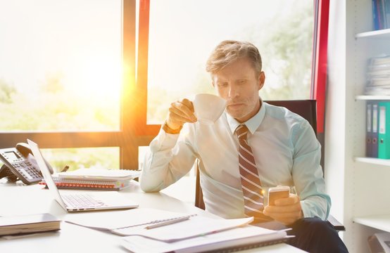 Mature businessman drinking coffee while reading file in office