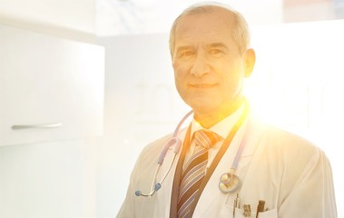 Portrait of Confident smiling senior dentist at dental clinic with yellow lens flare in background © MDBPIXS