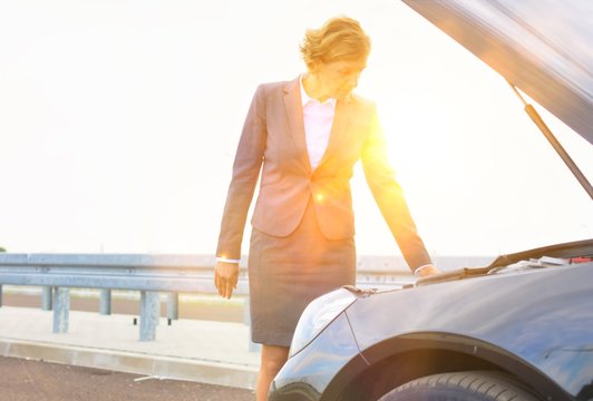 Mature businesswoman looking at breakdown car on road