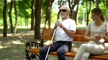 Blind old man sitting on bench near impolite disgruntled girl, human ignorance