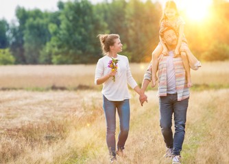 Fototapeta premium Father carrying his daughter on shoulders while walking with his wife in field