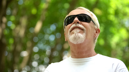 Smiling man in black sunglasses enjoying beautiful nature in park, resting