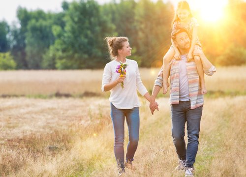 Father carrying his daughter on shoulders while walking with his wife in field