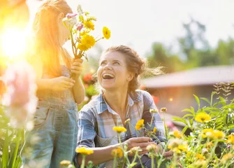 Fotobehang Mother and daughter picking pretty colourful flowers in their organic garden with yellow lens flare in background © moodboard