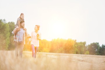 Happy family walking in wheat field with yellow lens flare in background