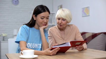 Mature woman showing female volunteer photo album, nursing home leisure, care
