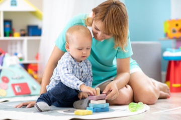 Happy mother and adorable baby boy playing on floor mat in sunny nursery room. Cute child with...