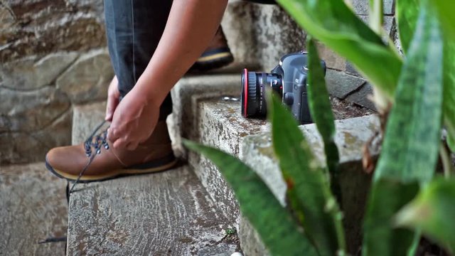 male tying shoelaces hiking boots with camera