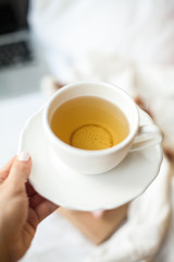 Close-up. Female hands hold a white cup of tea on the background of the bed. Cozy. Autumn. Winter.