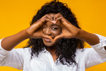 Cheerful african young woman shaping hands as heart on camera