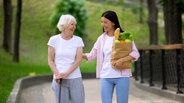 Granddaughter bringing food to elderly female patient, walking in hospital park