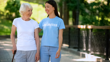 Smiling woman volunteer t-shirt and happy aged lady walking nursing home garden