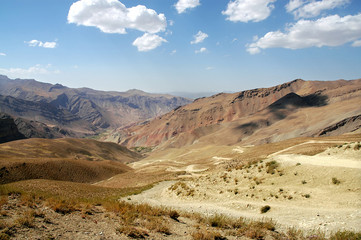 Naklejka na ściany i meble Between Chaghcharan and the Minaret of Jam, Ghor Province in Afghanistan. A view of a dirt road snaking down into a valley in a remote part of Central Afghanistan near Chaghcharan. Afghan landscape.
