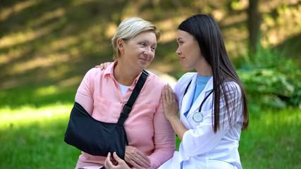 Caring female doctor hugging aged patient with arm sling, trauma rehabilitation