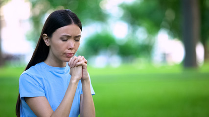 Fototapeta na wymiar Concentrated young woman praying outdoors closed eyes, spiritual support, wish