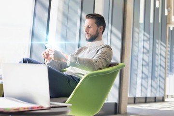 Businessman sitting while using smartphone in lobby