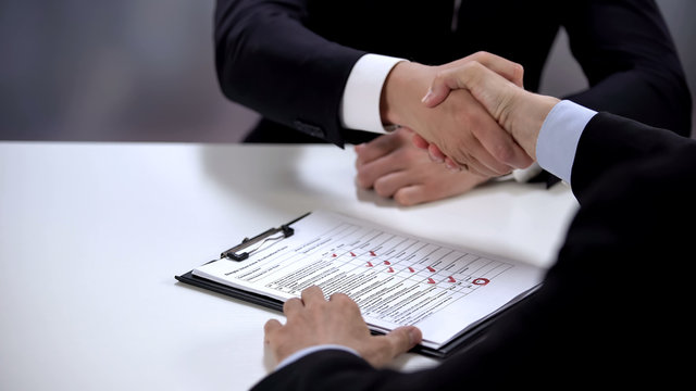 Boss and employee shaking hands, job candidate test lying on table, application
