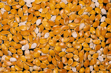 Shiny wet orange and white pumpkin seeds on a black background