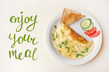 Enjoy your meal, handwritten lettering. Omelet with cheese and parsley, sliced vegetables on the plate. Scrambled eggs top view. Healthy nutrition. Inspirational quote, motivational phrase.