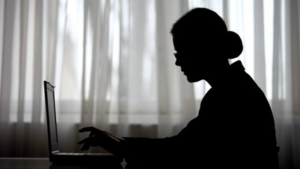 Silhouette of businesswoman working on laptop in early morning, meeting deadline