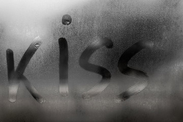 Kiss inscription painted on sweaty glass on rainy autumn day, Condensation and steam on window in cold autumn weather, valentines day concept