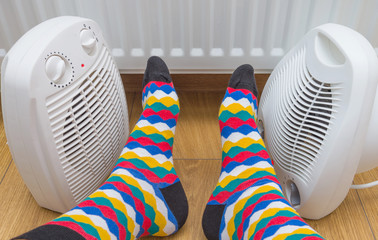 Feet in bright multicolored socks near heaters at home. Symbolic image of home heating in the cold...