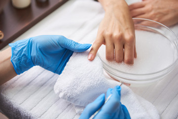 Young woman soaking hand in nail bath while manicurist holding her finger