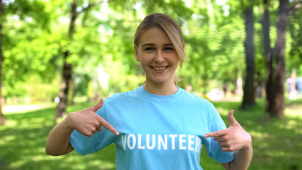 Smiling female pointing at volunteer word on t-shirt, forest conservation, earth