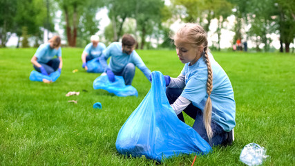 School girl with group of eco volunteers picking up litter park, saving nature