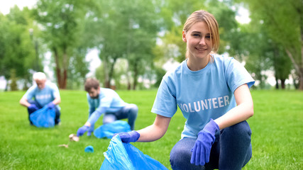 Pretty smiling female collecting forest garbage, looking at camera, volunteering