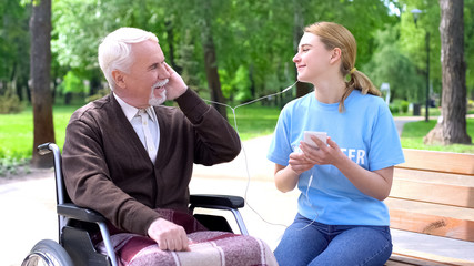 Happy young woman listening to music with old disabled man, supporting patient