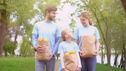 Volunteers family holding paper bags with fruits outdoors, feeding homeless
