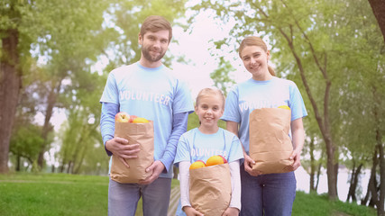Fototapeta premium Male female and child volunteers holding paper bags with fruits, smiling camera