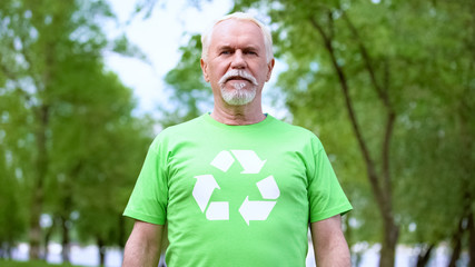 Naklejka na ściany i meble Senior man wearing recycling symbol t-shirt looking at camera, forest background