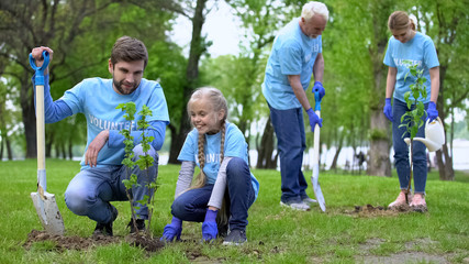 Happy volunteers family planting tree saplings outdoors, enjoying made work