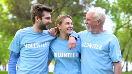 Three cheerful activists in volunteer t-shirts hugging, eco project achievement