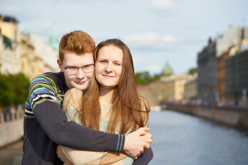 portrait of happy couple embracing in downtown, red-haired man with glasses, woman with long hair looking straight