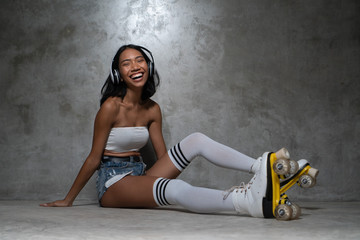 Young beautiful Asian girl in retro quads roller skates posing in studio over concrete wall background © stryjek