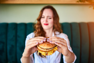 Pretty woman is refusing to eat unhealthy hamburger. She is looking at it with disgust