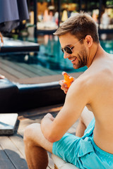 shirtless man sitting on lounger and applying sunscreen at resort