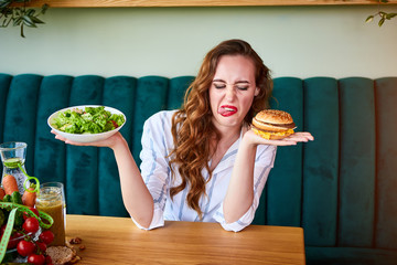 Pretty woman is refusing to eat unhealthy hamburger. She is looking at it with disgust