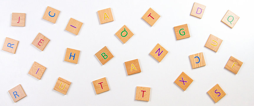Scattered alphabet letters wooden blocks tiles on white table background. Top view