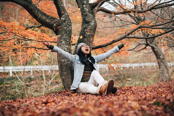 Portrait of woman sitting under maple tree and enjoy the autumn season by throwing maple leaves in the air.